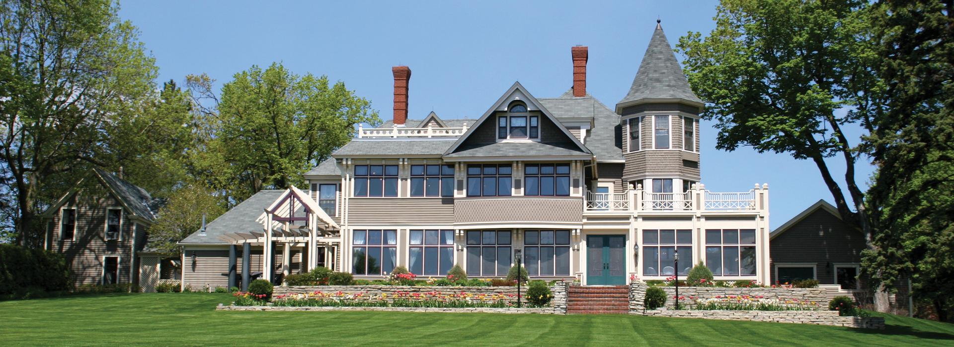 Colonial home with grey exterior, large windows, and manicured lawn with flowers